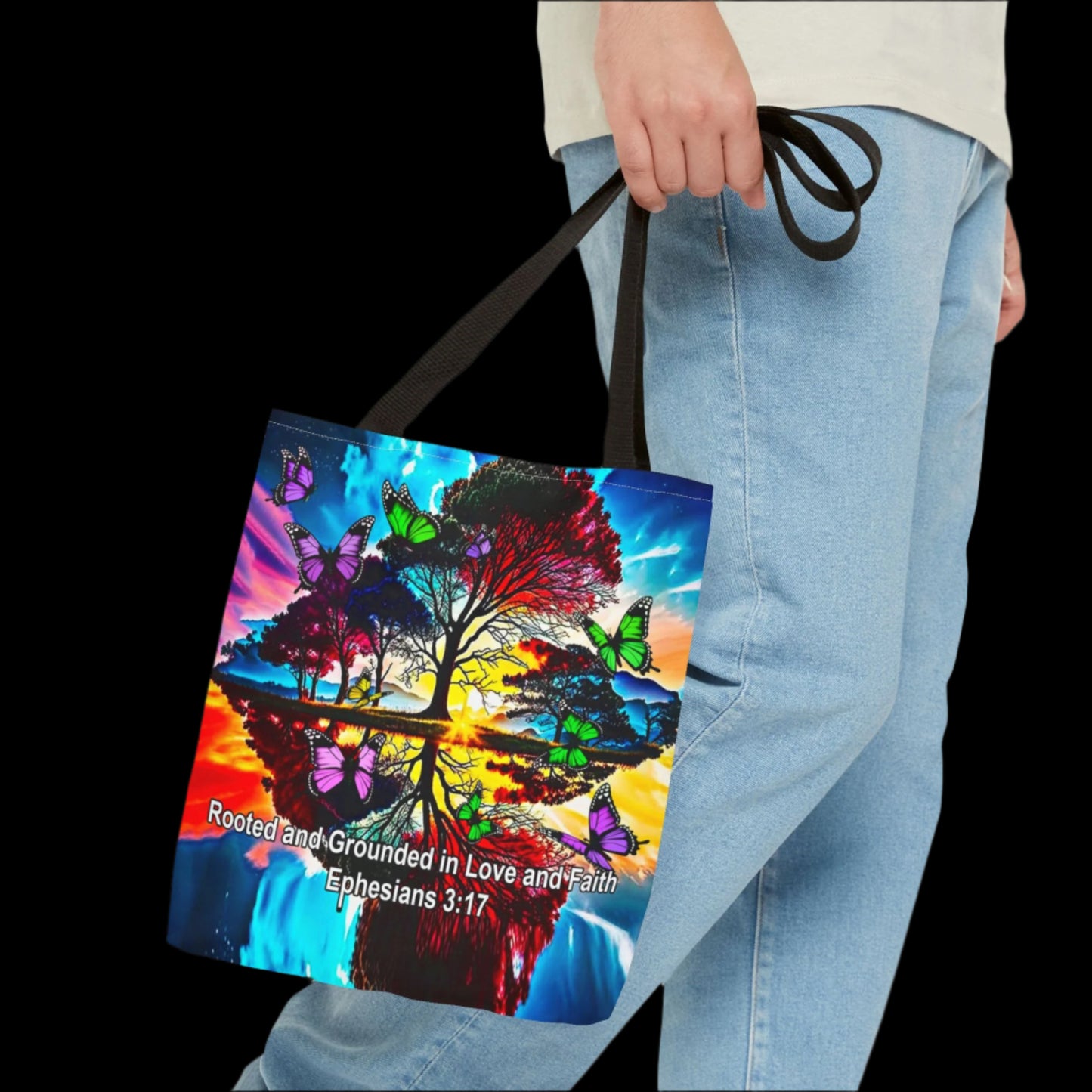 Tote bag with a colorful design of trees and butterflies held by a person wearing jeans.